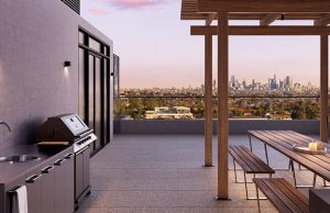 Stunning rooftop dining space complete with wooden pagola and benches for communal alfresco dining. The space features a built-in barbecue and sink space with panoramic views of the Melbourne city skyline